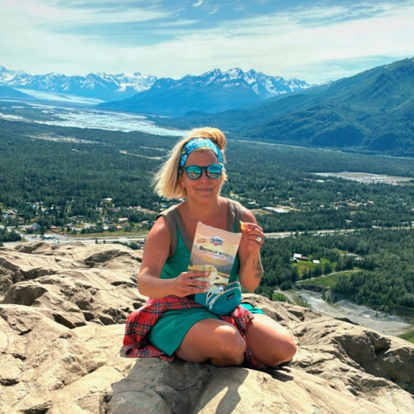 Woman sitting on a rocky mountain top with scenic view and mountains in the background